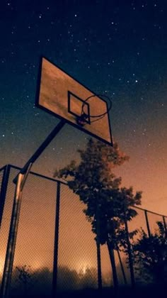 a basketball hoop in front of a fence with the night sky and stars above it