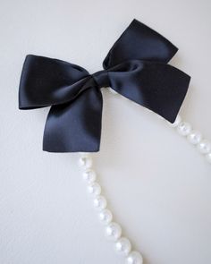 A classic pearl necklace with a dainty satin bow definitely to add an effortless romantic and classic look to your formal or casual style. Perfect to complete your date night, wedding, bridesmaids, holiday party, and any special occasions. This necklace is elastic and consists of assorted sizes of pearls. The bow can be styled sideways or at the back, or turn it around for another way to wear it. DETAILS: HANDMADEIMPORTED MATERIALS Elegant Adjustable Pearl Necklace For Evening, Elegant Adjustable Pearl Necklace For Formal Occasions, Elegant Black Pearl Necklace For Weddings, Classic Adjustable Necklaces For Party, Elegant Ribbon Necklaces For Evening, Elegant Bow Necklace For Party, Elegant Party Necklace With Bow, Elegant Evening Necklaces With Ribbon, Elegant Evening Necklace With Ribbon