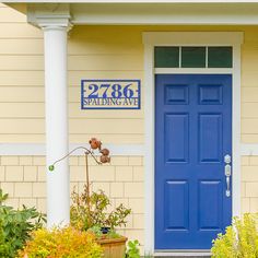 a blue front door on a yellow house with white pillars and flowers in the foreground