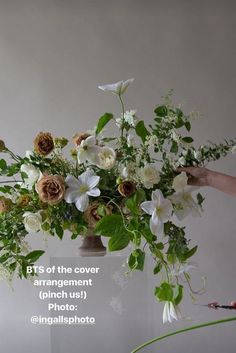 a person holding a vase with flowers in it and the words bts of the cover arrangement pitch us @ inadisphoto