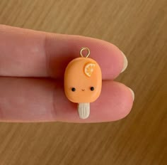 a tiny orange charm sitting on top of a person's finger in front of a wooden table