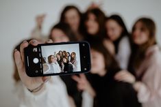 a woman taking a photo with her cell phone in front of a group of women