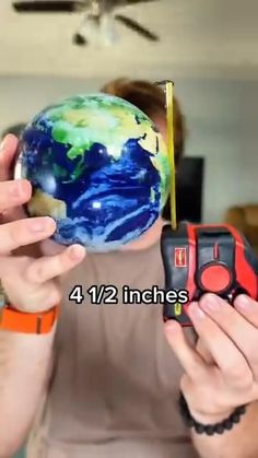 a man holding a small earth in his hands and measuring it with a tape measure