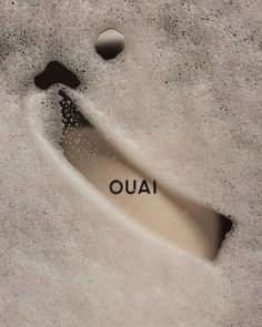 the word ouai written in sand next to two rocks and a small drop of water