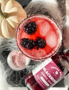 a close up of a drink in a glass with blackberries on the rim next to other drinks