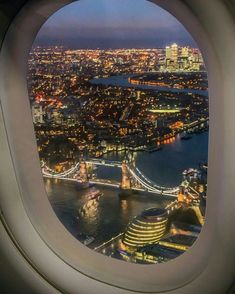 an airplane window looking out at the city lights and bridge across the river from london, england