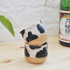 three black and white cups sitting on top of a wooden table next to a bottle