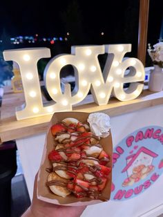 someone is holding up some food in front of a love sign at the fairground