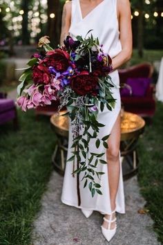 a woman in a white dress holding a bouquet with purple and red flowers on it