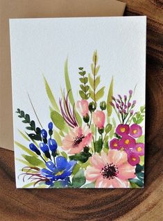 a card with watercolor flowers on it sitting on top of a piece of wood