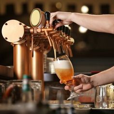 a person pours a glass of beer from a copper faucet at a bar