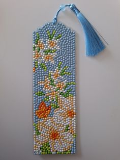 a beaded bookmark decorated with flowers and blue tasseled by a string