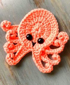 an orange crocheted octopus brooch with black eyes on a wooden surface,