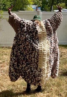 a man is standing in the grass with his arms out and two knitted sweaters hanging from him