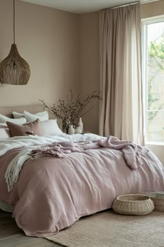 a bedroom with a large bed covered in pink blankets and pillows, along with a wicker basket on the floor