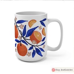 a white coffee mug with oranges and blue leaves on the outside, in front of a white background