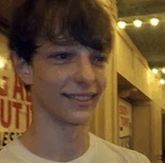 a young man smiling in front of a store with lights on the wall behind him