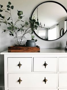 a white dresser topped with a mirror next to a potted plant on top of it