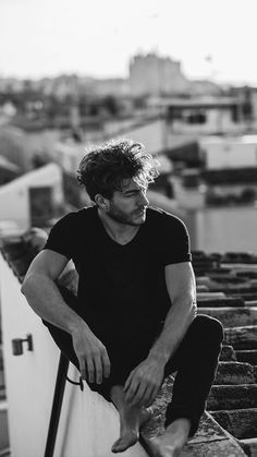 a man sitting on top of a roof with his legs crossed and looking off into the distance