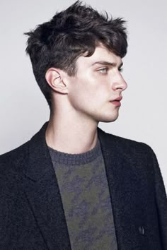 a young man in a black jacket and grey sweater looking off to the side with his head tilted