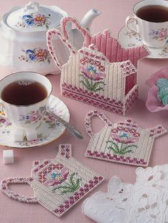 tea cups and coasters are sitting on a pink tablecloth with lace doily