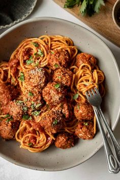 meatballs and spaghetti are served in a white bowl with a fork on the side