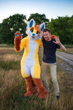 a man standing next to a fox mascot in the middle of a grass covered field