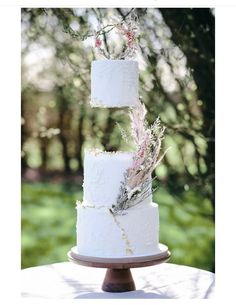 three tiered wedding cake with flowers on top and greenery in the middle, sitting on a table outdoors