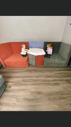 two small children sitting at a table in a living room with couches and chairs