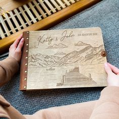 a person holding a wooden book with mountains in the background and writing that reads, kitty's journey