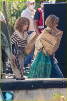 two people carrying bags and walking down the street with other people behind them, one holding a bag