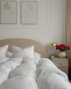 a bed with white comforter and pillows in a bedroom next to two pictures on the wall