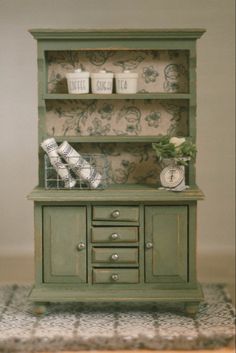 a green china cabinet sitting on top of a rug next to a wall mounted clock