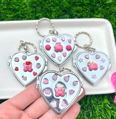 three heart shaped keychains with pigs and hearts on them, sitting in the grass