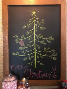 a chalkboard with a christmas tree drawn on it next to two jars filled with candy