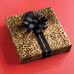 a gift wrapped in leopard print with a black ribbon and bow sits on a pink surface