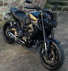 a black and gold motorcycle parked in front of a stone wall on the side of a road