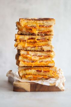 a stack of grilled cheese sandwiches sitting on top of a wooden cutting board next to a white wall