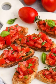 slices of toasted bread topped with tomatoes and basil on a white plate next to fresh cherry tomatoes