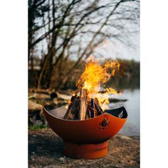 a fire pit sitting on top of a rock next to a body of water with trees in the background