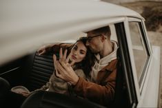 a man and woman sitting in the back seat of a car waving at each other