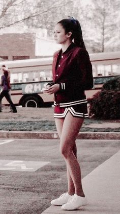 a young woman standing on the side of a road next to a parking lot with a school bus in the background