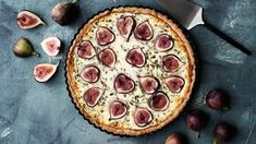 a pizza topped with sliced figs on top of a blue table next to a knife