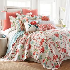 a bed with red and white flowers on it in a room next to a window