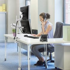 a woman sitting at a desk talking on her cell phone while using a desktop computer