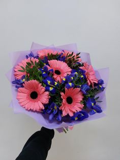 a hand holding a bouquet of pink and blue flowers