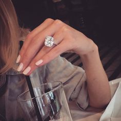 a woman is sitting at a table with a glass and a ring on her finger