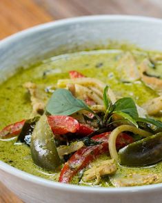 a white bowl filled with green soup on top of a wooden table