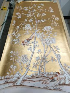 a painting is being worked on with gold paint and white flowers, while two birds are perched on the tree branch