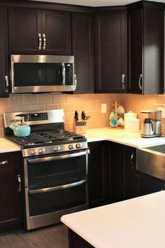 a kitchen with stainless steel appliances and dark wood cabinets, white counter tops and wooden flooring